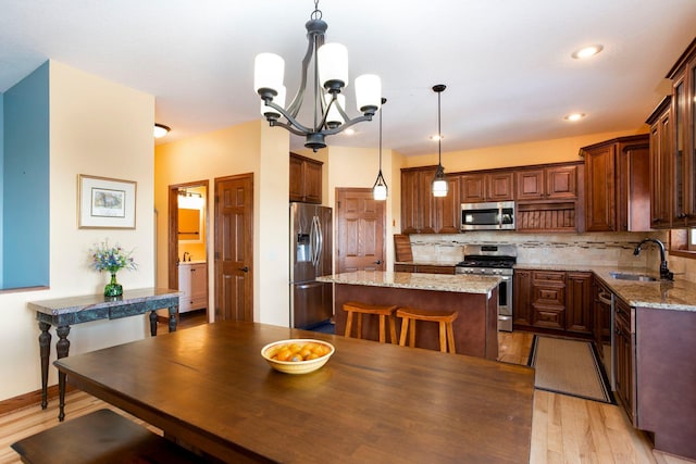 kitchen with light stone counters, a center island, decorative light fixtures, appliances with stainless steel finishes, and a sink