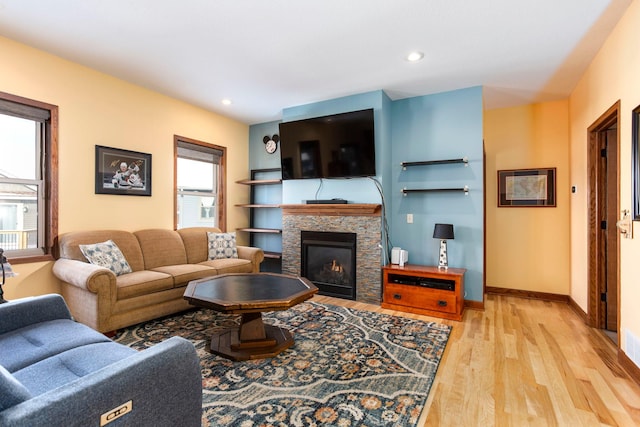 living area with light wood finished floors, a stone fireplace, a healthy amount of sunlight, and recessed lighting