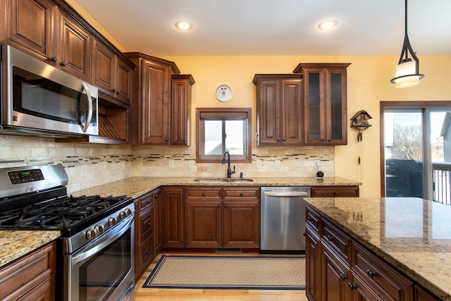 kitchen with hanging light fixtures, a sink, tasteful backsplash, appliances with stainless steel finishes, and light stone counters