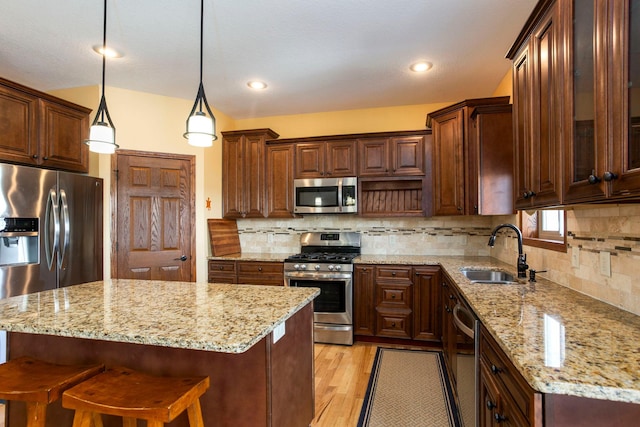 kitchen with a sink, stainless steel appliances, light wood finished floors, decorative backsplash, and light stone countertops