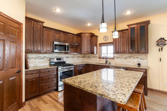 kitchen with a sink, stainless steel appliances, a breakfast bar, pendant lighting, and light wood finished floors