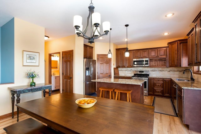 kitchen featuring a center island, light wood-style flooring, a sink, stainless steel appliances, and tasteful backsplash