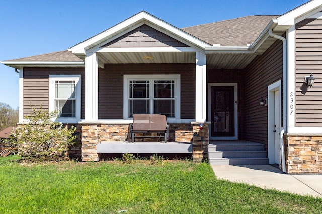 view of front facade with a shingled roof, a porch, a front yard, and stone siding