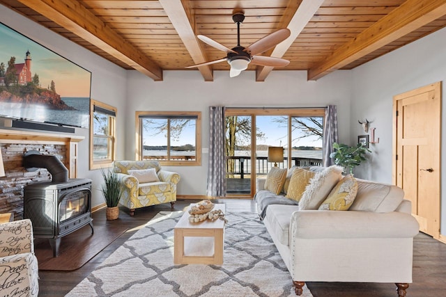 living area with wooden ceiling, wood finished floors, a ceiling fan, beamed ceiling, and a wood stove