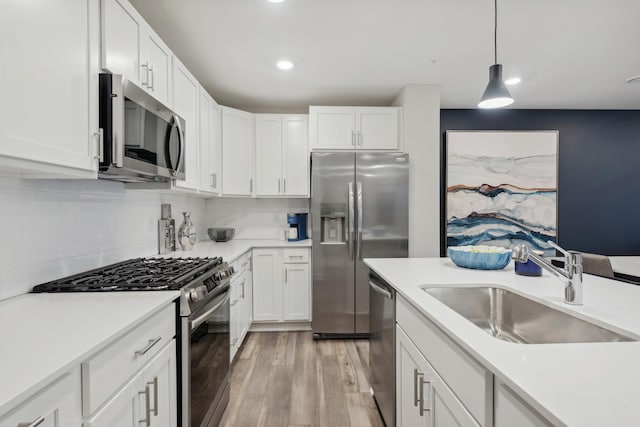 kitchen with white cabinetry, stainless steel appliances, sink, and hanging light fixtures