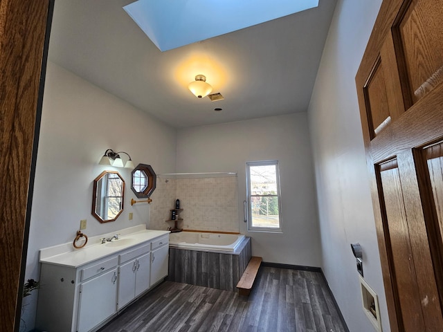 bathroom featuring a relaxing tiled tub, vanity, wood-type flooring, and a skylight