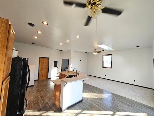 kitchen with sink, dark wood-type flooring, a breakfast bar area, black refrigerator, and a center island with sink