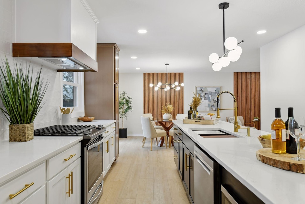 kitchen featuring decorative light fixtures, custom exhaust hood, sink, stainless steel appliances, and white cabinets