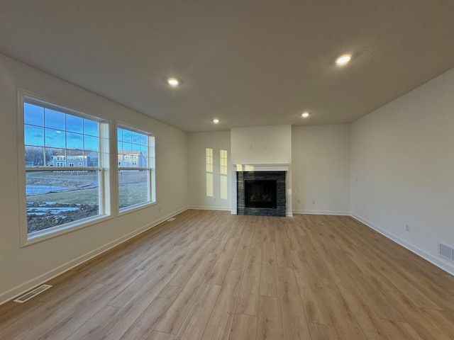 unfurnished living room with light hardwood / wood-style floors and a stone fireplace