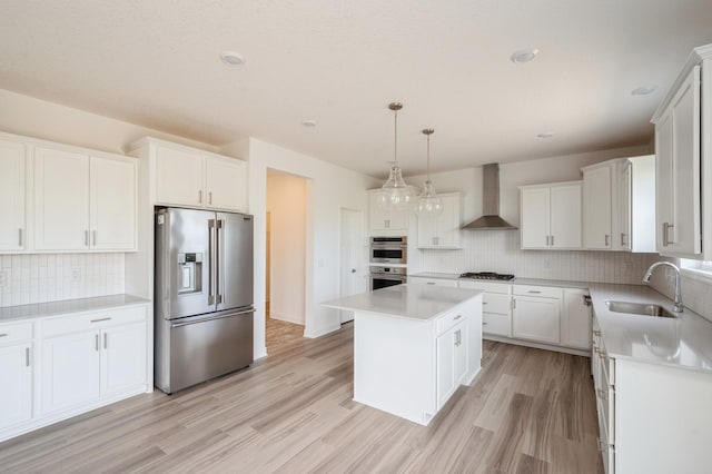 kitchen featuring sink, wall chimney exhaust hood, a kitchen island, white cabinets, and appliances with stainless steel finishes