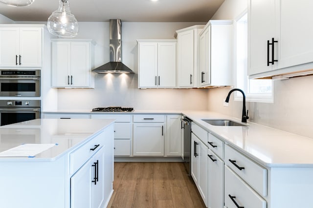 kitchen featuring appliances with stainless steel finishes, sink, white cabinets, hanging light fixtures, and wall chimney exhaust hood