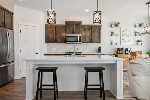 kitchen with decorative light fixtures, dark brown cabinets, stainless steel appliances, and a center island with sink