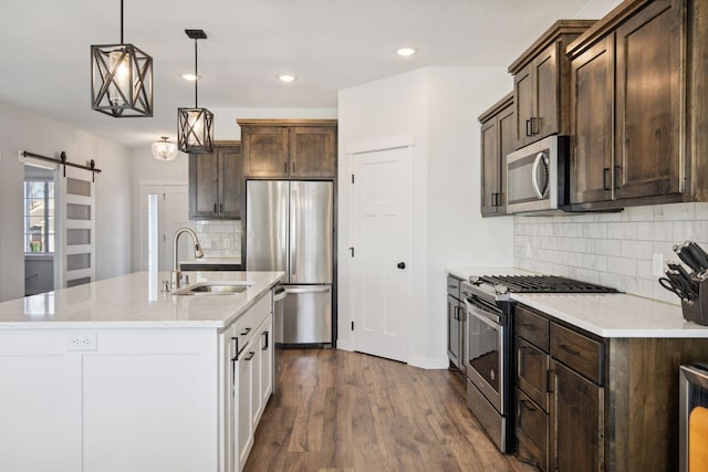 kitchen featuring decorative light fixtures, stainless steel appliances, sink, backsplash, and a barn door