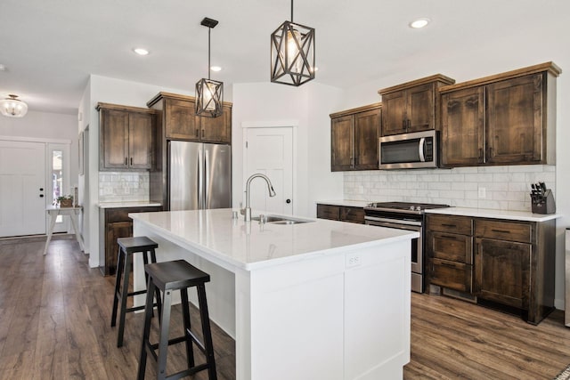 kitchen with hanging light fixtures, backsplash, appliances with stainless steel finishes, and an island with sink