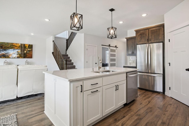 kitchen with a barn door, a center island with sink, appliances with stainless steel finishes, dark wood-type flooring, and sink