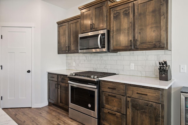 kitchen with wood-type flooring, appliances with stainless steel finishes, dark brown cabinets, and tasteful backsplash