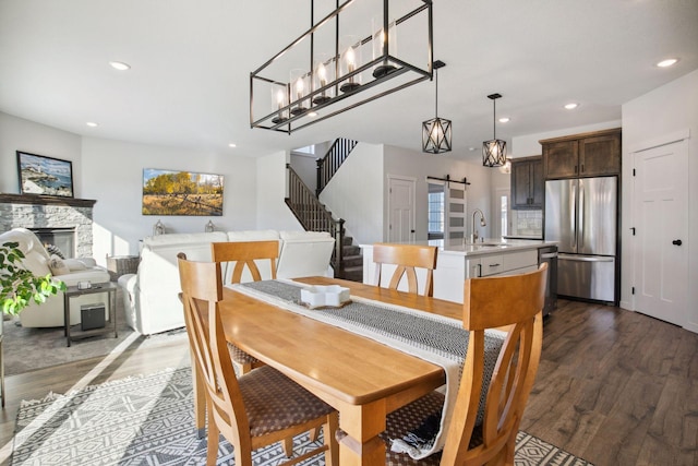 dining area with sink, dark hardwood / wood-style floors, a stone fireplace, and a barn door