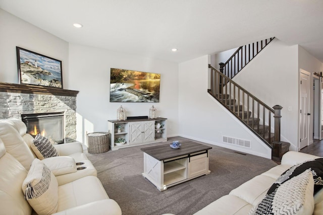 living room with a stone fireplace and dark colored carpet