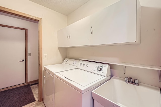 laundry room with sink, washing machine and clothes dryer, a textured ceiling, and cabinets