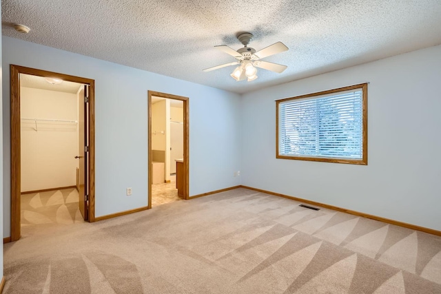 unfurnished bedroom featuring light carpet, ceiling fan, ensuite bath, a walk in closet, and a closet