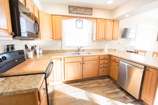 kitchen with light brown cabinetry, a breakfast bar, black appliances, light wood-type flooring, and sink