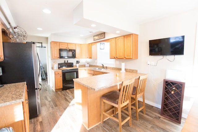 kitchen featuring kitchen peninsula, light wood-type flooring, black appliances, and sink