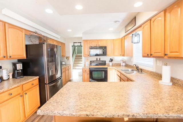 kitchen featuring black appliances, light wood-type flooring, kitchen peninsula, light brown cabinetry, and sink