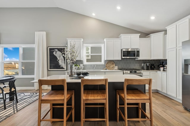 kitchen featuring a kitchen breakfast bar, stainless steel appliances, white cabinetry, and lofted ceiling