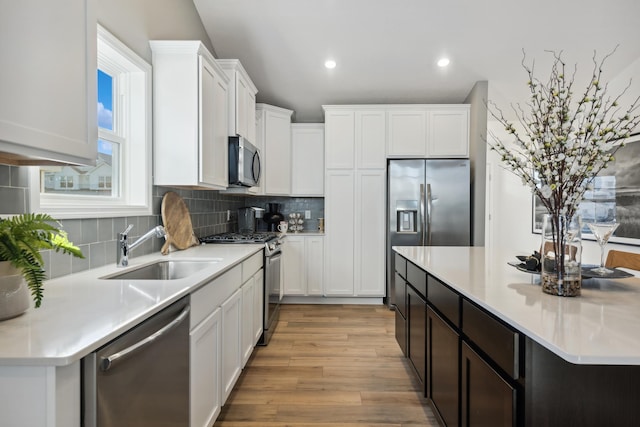 kitchen with tasteful backsplash, stainless steel appliances, sink, light hardwood / wood-style flooring, and white cabinetry