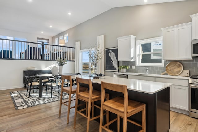 kitchen featuring light wood-type flooring, stainless steel appliances, sink, a center island, and white cabinetry