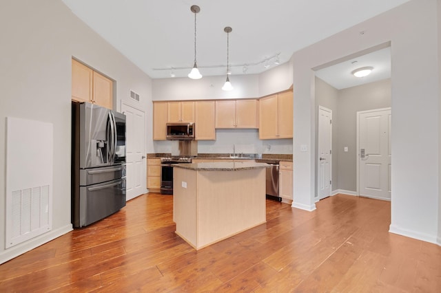 kitchen with sink, a center island, light stone counters, pendant lighting, and appliances with stainless steel finishes