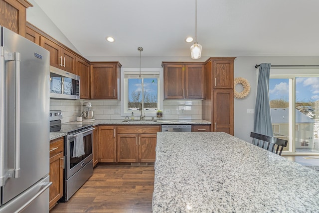 kitchen with appliances with stainless steel finishes, pendant lighting, decorative backsplash, and light stone counters