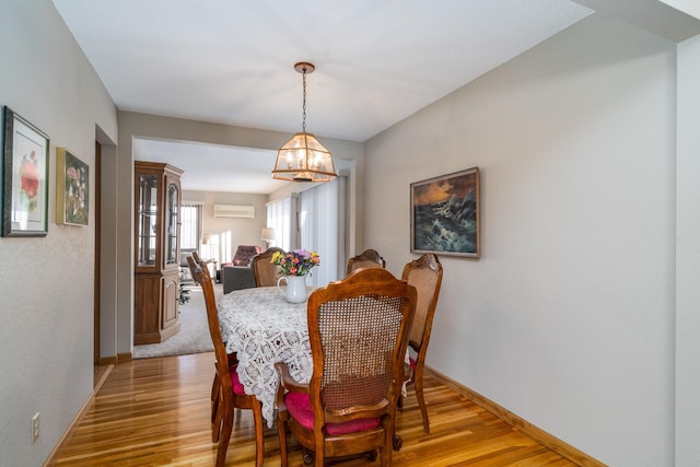 dining space with a chandelier, light wood-type flooring, and a wall unit AC