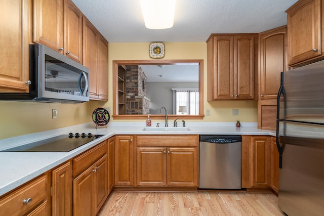 kitchen with a textured ceiling, sink, stainless steel appliances, and light hardwood / wood-style flooring