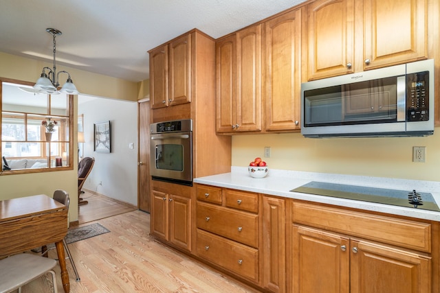 kitchen with hanging light fixtures, stainless steel appliances, light wood-type flooring, and a notable chandelier