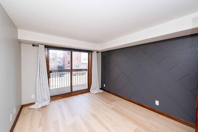 unfurnished room with light wood-type flooring, baseboards, and an accent wall