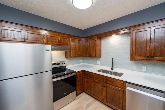 kitchen with a sink, light countertops, under cabinet range hood, appliances with stainless steel finishes, and tasteful backsplash