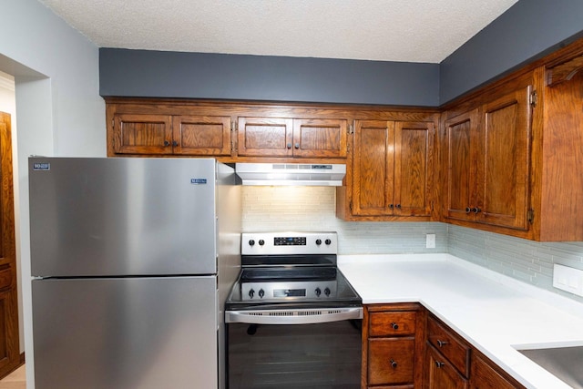 kitchen featuring brown cabinets, under cabinet range hood, stainless steel appliances, light countertops, and decorative backsplash