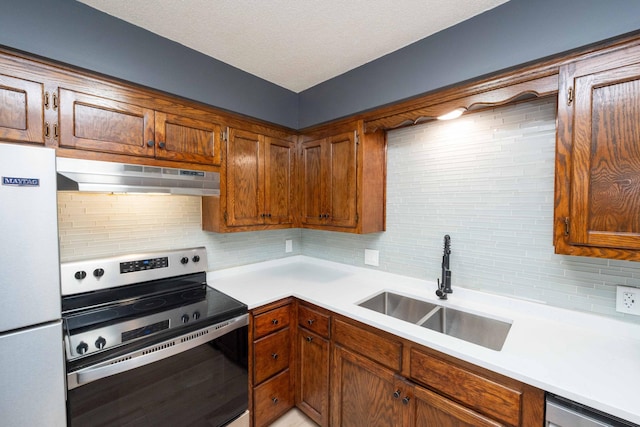 kitchen featuring under cabinet range hood, light countertops, decorative backsplash, stainless steel appliances, and a sink