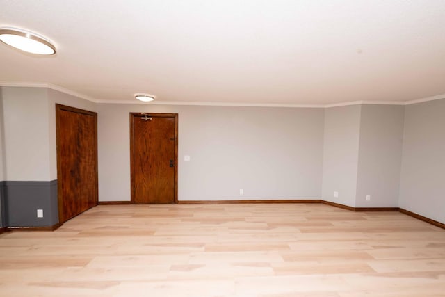 empty room featuring light wood finished floors, crown molding, and baseboards