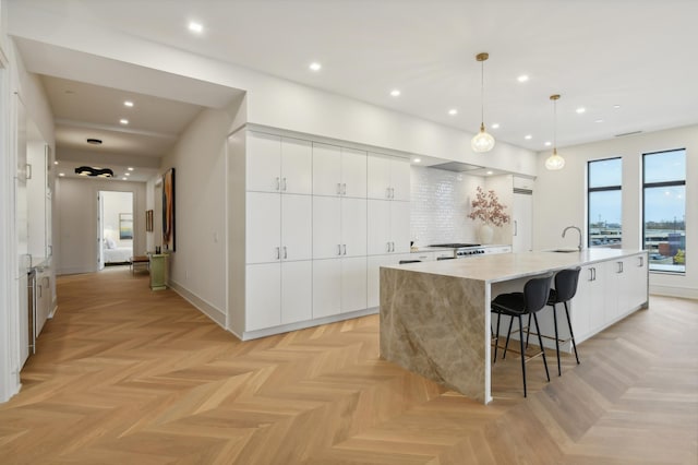 kitchen featuring a large island with sink, white cabinetry, pendant lighting, and light parquet floors