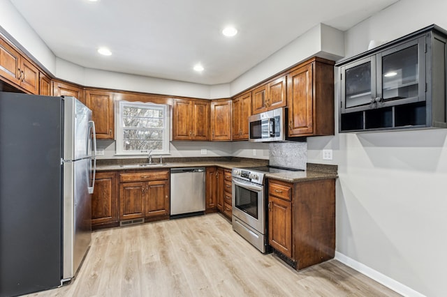 kitchen with sink, light hardwood / wood-style flooring, stainless steel appliances, and dark stone counters