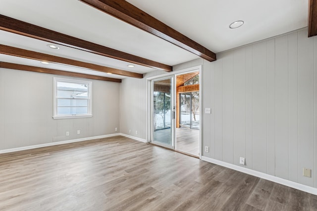 empty room with light hardwood / wood-style flooring, wood walls, and beamed ceiling