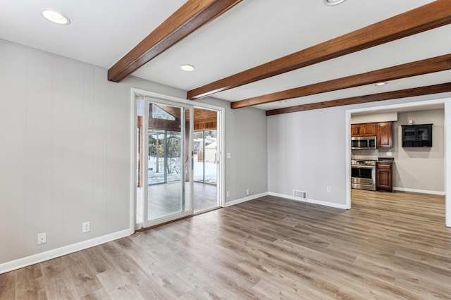 unfurnished living room with beamed ceiling and light wood-type flooring