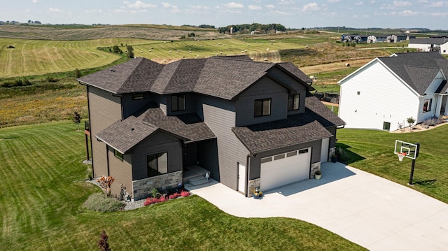 view of front facade with a shingled roof, concrete driveway, a rural view, and stone siding