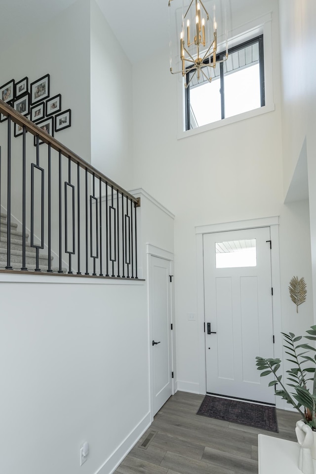 foyer with dark wood-type flooring, a towering ceiling, baseboards, stairs, and an inviting chandelier