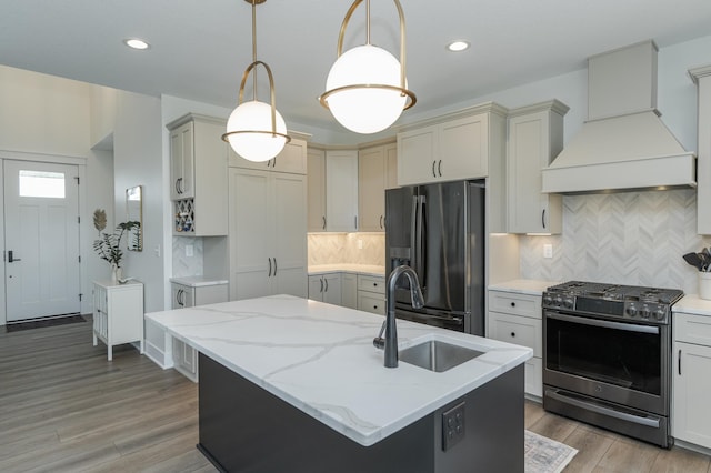 kitchen featuring black fridge, an island with sink, custom exhaust hood, and gas range