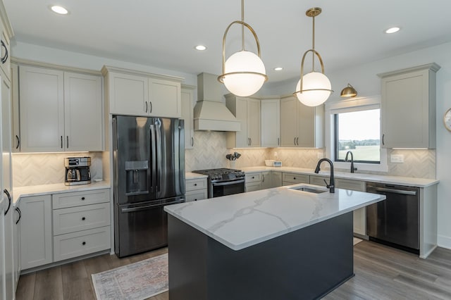 kitchen featuring custom range hood, light stone counters, decorative light fixtures, a kitchen island with sink, and stainless steel appliances