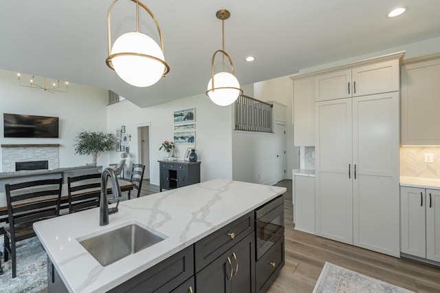 kitchen with light stone counters, a kitchen island with sink, a sink, hanging light fixtures, and built in microwave