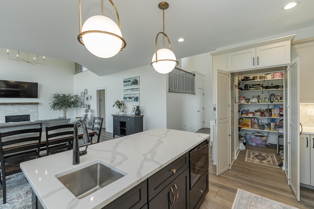 kitchen with light stone counters, decorative light fixtures, built in microwave, a sink, and light wood-type flooring